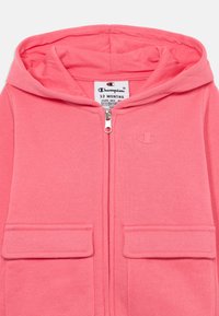 Svijetloružičasta zip-up dukserica za dojenčad, sa kapuljačom, dva prednja džepa i logotipom na lijevoj strani grudi. Izrađena od mekanog, udobnog materijala.