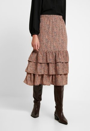 Jupe midi à motif floral marron avec trois volants, taille élastique, portée avec des bottes en cuir marron brillantes montantes jusqu'au genou.