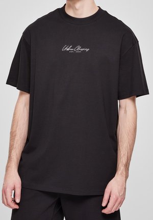 Sort oversized T-shirt med korte ærmer og hvid "Urban Classics EST. 2005" tekst på brystet, båret af en stående person.