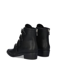 Botas de cuero negro hasta el tobillo con punta afilada, con tres hebillas decorativas y cremalleras laterales. Tacón bajo apilado y textura suave.
