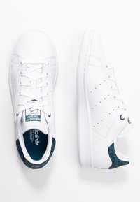 Zapatillas de cuero blanco con detalles perforados, cordones planos y un forro de estampado de leopardo azul alrededor del collar y la lengua.