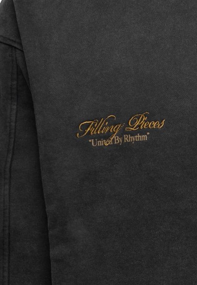 Schwarzer Sweatshirt mit weicher Textur, auf der Vorderseite mit goldenen, gestickten Schriftzügen "Filling Pieces" und "United By Rhythm".