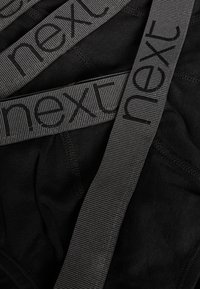 Schwarze Unterwäsche mit einem strukturierten, grauen elastischen Bund, auf dem das Wort "next" in dunklen Buchstaben geprägt ist. Glattes Material insgesamt.
