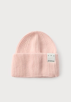 Bonnet en maille côtelée rose clair avec revers et étiquette rectangulaire blanche indiquant "CPH STUDIOS" sur un fond clair uni.