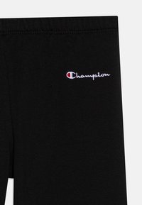 Leggings de sport noirs en tissu mélangé coton avec une taille élastique. Présente un logo "Champion" brodé en blanc sur la cuisse gauche.