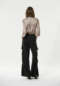 Braun gemusterte Bluse mit plissiertem Rücken, kombiniert mit schwarzen Cargo-Hosen im Stil mit Seitentaschen und weit ausgestellten Säumen.