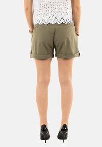 Pantalones cortos verde oliva hechos de un tejido ligero, con puños enrollados y bolsillos laterales, combinados con zapatos de tacón alto negros.