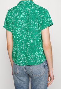 Grünes Kurzarmhemd mit floralem und gepunktetem Muster, aus leichtem Stoff gefertigt, mit Button-Down-Kragen und abgerundetem Saum.