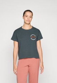 Dark green cropped t-shirt with a round neckline and short sleeves; features a printed graphic in orange and white reading "PEACEFUL."