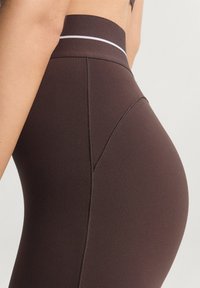 High-waisted brown leggings with a smooth texture, featuring a contrasting white accent at the waistband and seam detailing.