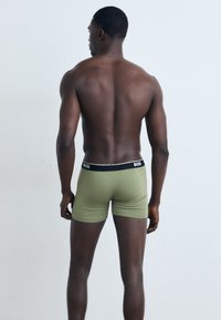 Grüne Boxershorts mit einem schwarzen Bund, der das "BOSS"-Logo zeigt, enganliegendes Design und glatte Textur, von hinten präsentiert.