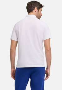 Witte poloshirt met korte mouwen, gladde structuur en een klassieke kraag. Draag het met een blauwe broek, gezien van de achterkant.