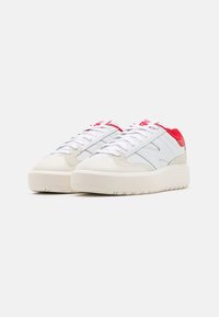 Białe sneakersy z fakturowaną, off-white podeszwą, z czerwonymi akcentami na pięcie i języku oraz szarymi skórzanymi panelami bocznymi.