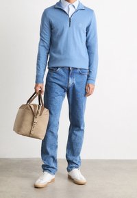 Pull bleu clair avec un col zippé, jean bleu, sac beige avec des accents en cuir marron, et baskets blanches avec une semelle gomme.
