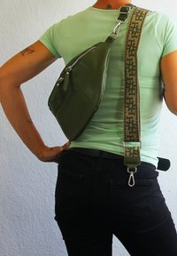 Sac en cuir vert en bandoulière avec une finition texturée, doté d'une fermeture éclair en argent. La sangle est à motifs beige et vert avec un fermoir en métal.