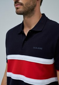 Námořnické polo tričko s horizontálními červenými a bílými pruhy, texturovaná tkanina a logo "Salsa Jeans" na prsou. Klasický design límce.