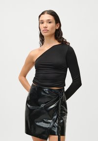 Fekete, egy vállat fedő top rugalmas anyagból, ráncolt részletekkel és testhezálló fazonnal. Fényes fekete bőrnadrággal kombinálva, ami mini hosszt képvisel.