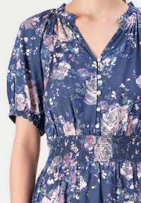Robe bleue à motifs floraux avec des manches bouffantes, taille élastique froncée et boutons blancs sur le devant au niveau du col.