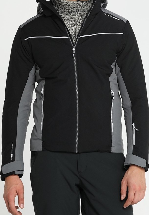 Mann trägt eine schwarze und graue Winterjacke mit Reißverschlüssen und ein gemustertes Rollkragenpullover darunter.
