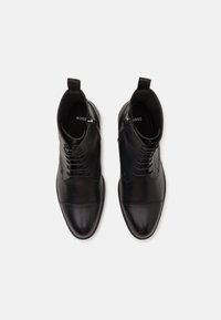 Botas de tobillo de cuero negro con un acabado pulido y elegante, que cuentan con cordones, una lengüeta y un sutil logotipo en la plantilla.