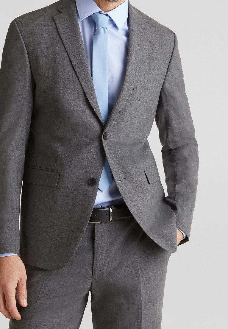 Completo grigio con vestibilità slim e revers a punta, abbinato a una camicia dress azzurra chiara e una cravatta coordinata. Una cintura nera accentua il look.