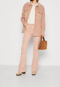 Vaaleanpunainen villasekoite takki, jossa on kaksi taskua, valkoinen paita, vaaleanpunaiset leveälahkeiset farkut, beiget platform-kengät ja ruskea mokkanahkainen käsilaukku.