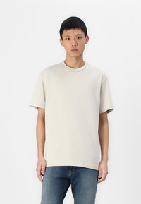 Beige bomulds t-shirt med rund hals og korte ærmer, med et diskret broderet logo på venstre bryst og en afslappet pasform.