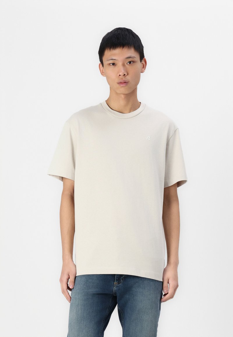 Beige bomulds t-shirt med rund hals og korte ærmer, med et diskret broderet logo på venstre bryst og en afslappet pasform.