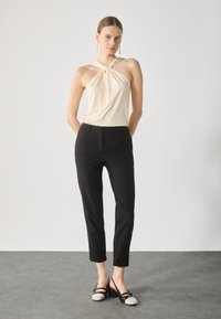 Top halter crema con dettagli in tessuto intrecciato, abbinato a pantaloni neri a gamba stretta. Le calzature presentano un design a blocchi di colore nero e crema.