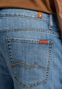 Jeans in denim azzurro chiaro caratterizzati da una tasca posteriore con un distintivo ricamo a ondina e un piccolo tag di marca vicino al punto vita.