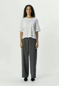 White short-sleeve top with a wave-patterned cutout design, paired with loose gray trousers and black footwear. Simple and modern silhouette.