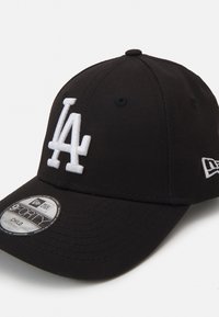 Juodas beisbolo kepuraitė, pagaminta iš medvilnės mišinio, su balta išsiuvinėta "LA" logotipu ir reguliuojamu dirželiu gale. Suformuotas dizainas.