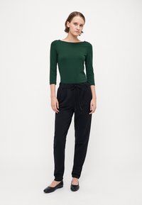 Grønn tettsittende langermet topp, svarte snøretruser og svarte leiligheter. Jevnt stoff, klassisk design og nøytral fargepalett.