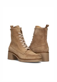 Une paire de bottines en daim beige avec des lacets à l'avant, des bouts ronds, des tirettes à l'arrière et des talons épais de hauteur moyenne.