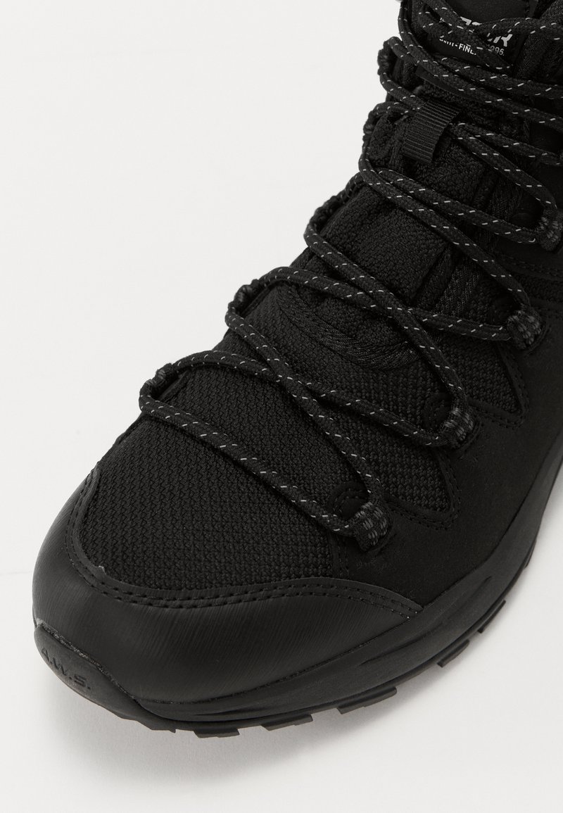 Schwarzer Wanderschuh mit einer strukturierten Stoff-Oberfläche, verstärkter Zehenkappe und schwarzen Schnürsenkeln mit einem reflektierenden Muster auf einer Gummisohle.