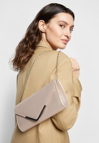 Pale pink clutch bag with a textured surface, triangular flap, and black metallic accent. Features a chain strap for crossbody or clutch use.