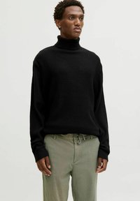 Black turtleneck sweater with a textured, ribbed pattern and long sleeves, paired with light green trousers featuring a drawstring waist.