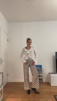 Weißes Blusenshirt mit schwarzen Rüschendetails, kombiniert mit hoch taillierten, weit geschnittenen Hosen mit einem schwarz-weißen abstrakten Muster. Schwarze High Heels.
