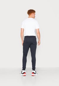 Marine joggers med en afslappet pasform, elastisk talje og baglomme, parret med en simpel hvid t-shirt og sporty fodtøj.