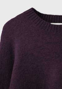 Gros plan d'un pull en tricot violet foncé montrant l'encolure ronde côtelée et le tissu doux et texturé.