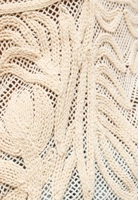 Πλεκτό ύφασμα σε κρεμ απόχρωση με ανάγλυφα λουλουδένια και φυλλώδη σχέδια πάνω σε δαντελωτό φόντο, που παρουσιάζει υφή νήματος και ανοιχτό σχέδιο.