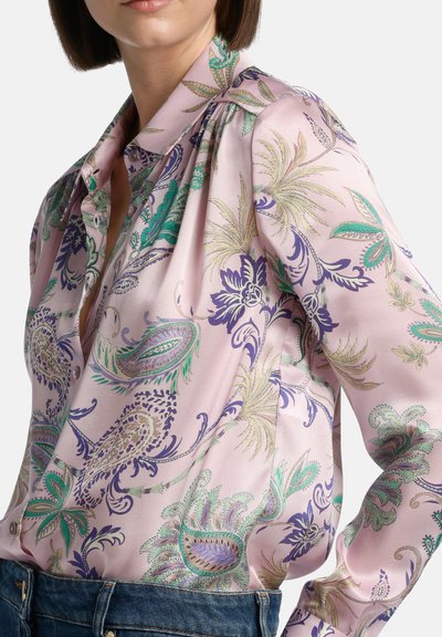 Silkkipusero pehmeässä vaaleanpunaisessa värissä, jossa on elävät vihreät ja purppurat paisley-kuviot. Puserossa on napitettava malli ja pitkät hihat. Teksturoitu pinta.