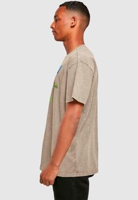 Graues T-Shirt mit Rundhalsausschnitt und kurzen Ärmeln, das blaue und grüne grafische Akzente aufweist. Weicher, abgenutzter Stoff mit sichtbaren Nähdetails.