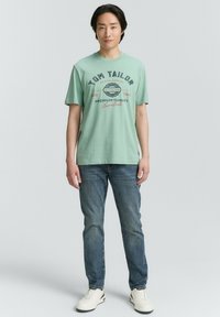 Mėtų žalios spalvos medvilninės marškinėliai su atspausdintu užrašu "TOM TAILOR" ir "PREMIUM QUALITY" tamsiai mėlyna ir raudona spalvomis. Derinama su mėlynomis džinsinėmis kelnėmis ir baltomis sportbačiais.