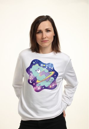 Biała bluza z kapturem z nadrukiem rysunkowego niedźwiedzia w kosmosie, trzymającego fioletową planetę, otoczonego gwiazdami i księżycami na kolorowym tle galaktyki.