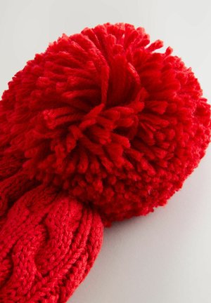 Piros kötött sál, amely textúrált kötélmintával rendelkezik, és az egyik végén egy nagy, bolyhos pom-pom található, lágy, vastag megjelenést kölcsönözve.