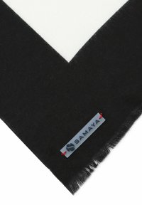 Black fabric with a frayed edge featuring a rectangular tag attached by red thread, displaying the brand name "Samaya" and a logo.