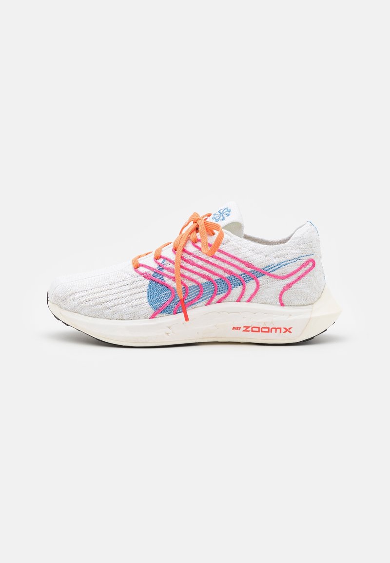 Baskets de sport blanches avec des lacets orange, des motifs de vagues bleus et roses, et une épaisse semelle blanche portant l'inscription "Nike ZoomX" sur un fond uni.