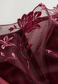 Țesătură de dantelă burgundă cu broderie florală și textură ridicată. Marginile delicate cu formă de semilună și detaliile complexe adaugă un interes vizual.