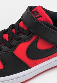 Sort og rød sneaker med en glat læderoverdel, kontrastsyede sømme, polstret krave og en hvid gummisål med et Nike-logo.